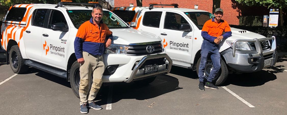 Two Pinpoint workers standing in front of branded Pinpoint utes