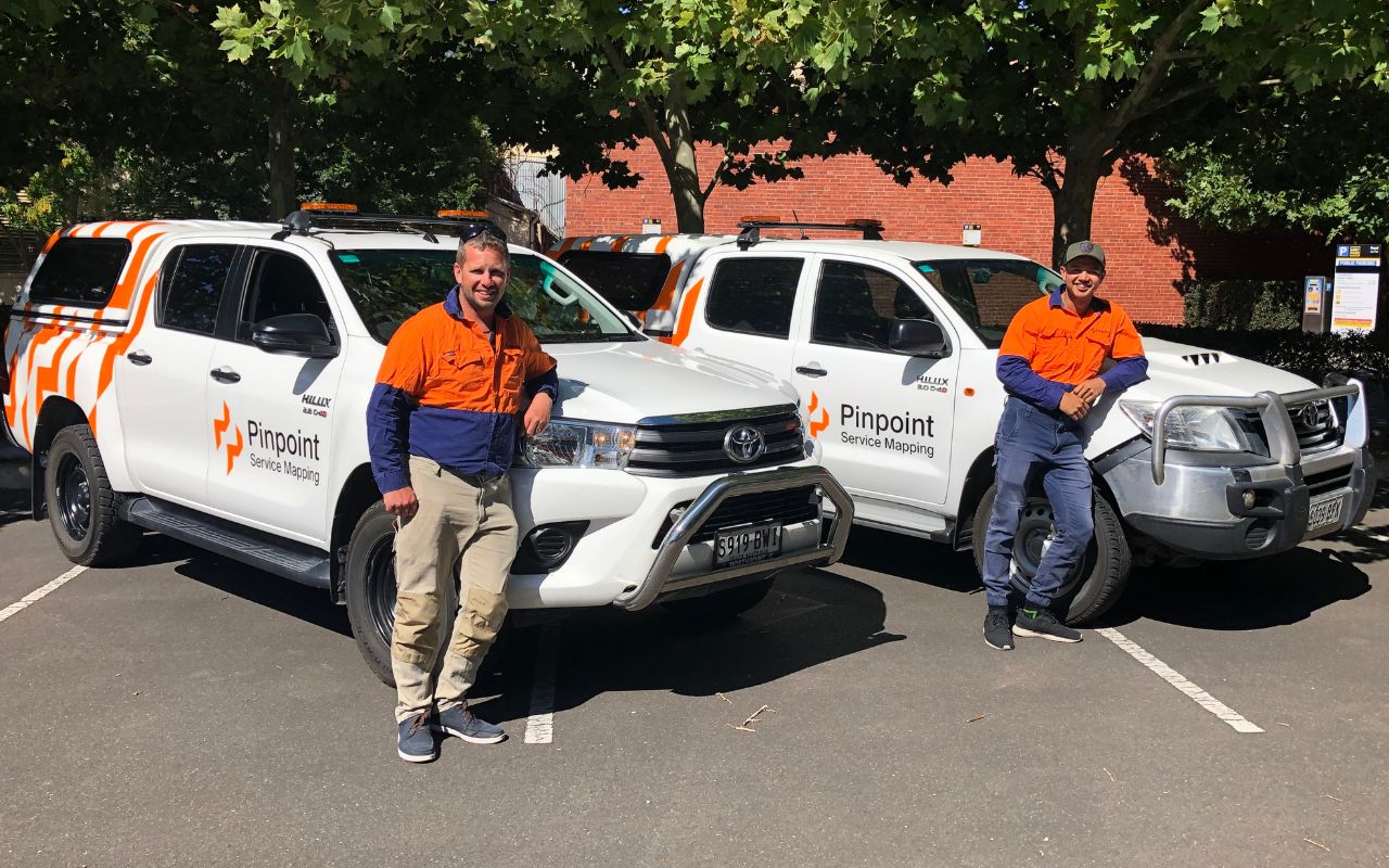 Two Pinpoint workers standing in front of branded Pinpoint utes